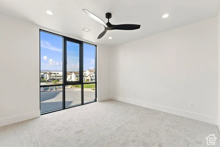 Expansive floor-to-ceiling windows, modern ceiling fan, recessed lighting, neutral carpeting, and white walls