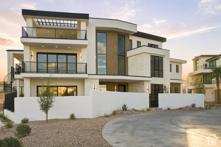 Modern exterior architecture featuring a flat roofline, multiple balconies with black railings, a spiral staircase, stone veneer accents, and large windows