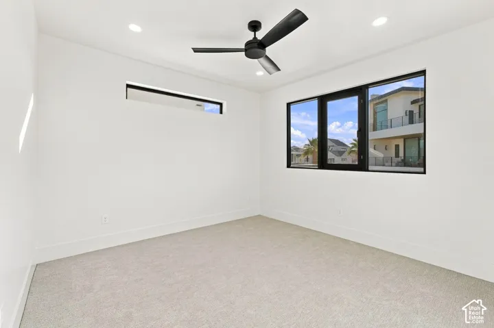 Recessed lighting, a modern black ceiling fan, and black-framed windows complement the light-toned carpet