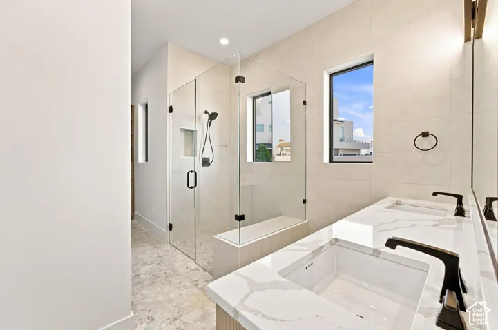 Dual basin vanity with quartz countertops, walk-in shower with glass enclosure, integrated shower bench, and dark-finish fixtures