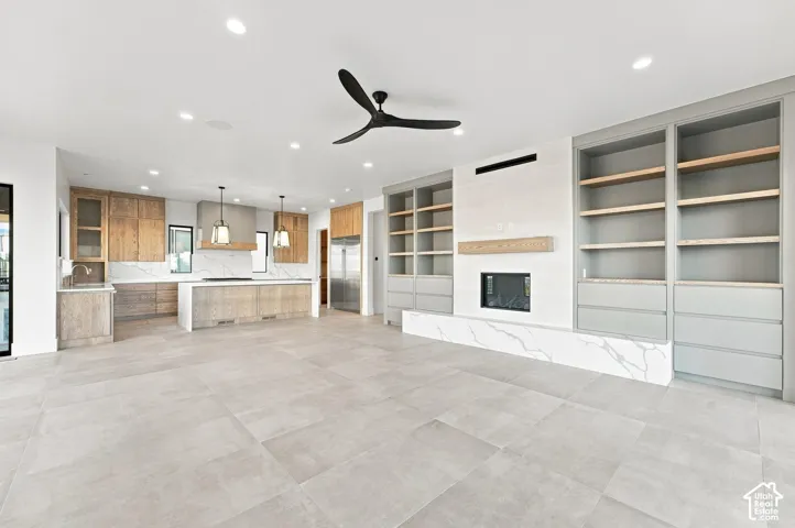 Expansive open-concept living space featuring large format tile flooring, a built-in electric fireplace with a substantial hearth, custom built-in cabinetry, and a kitchen with wood-finish cabinetry and pendant lighting