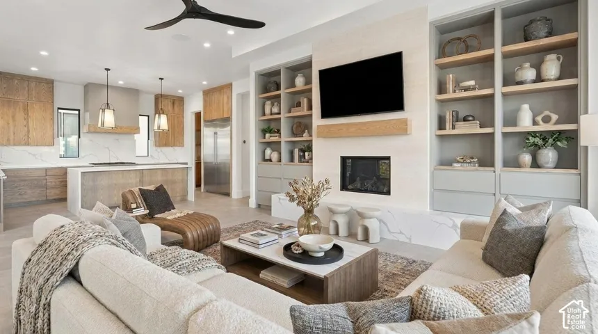 Open-concept living area featuring a built-in fireplace, custom shelving, a gourmet kitchen with an expansive island, and recessed lighting throughout