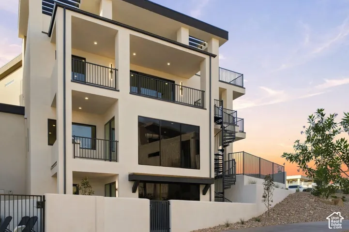 Multi-story stucco exterior with multiple balconies, a spiral staircase, large windows, and black metal railings