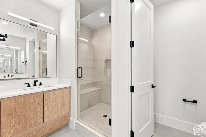Contemporary bathroom featuring a wood-finish vanity with a white countertop and rectangular sink, a frameless shower with tile surround and built-in bench, and matte black hardware