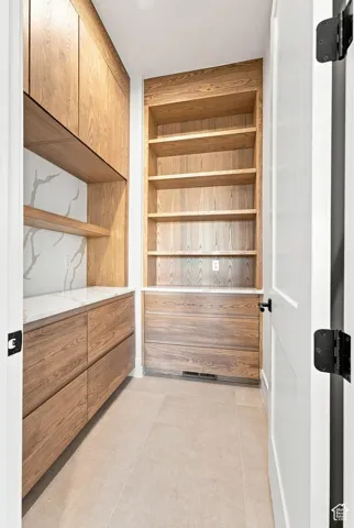 Built-in wood-finish cabinetry, integrated open shelving, solid surface countertops, and neutral tile flooring