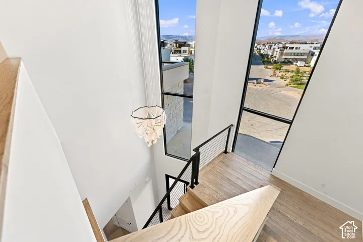 Hardwood stairs with cable railing, modern chandelier, and expansive vertical windows