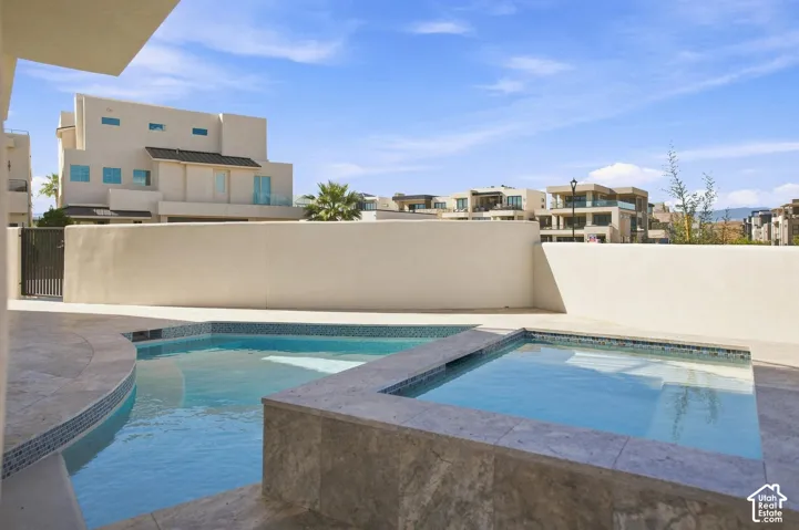 Curved swimming pool with integrated spa and mosaic tile accents, surrounded by a light-toned stucco wall