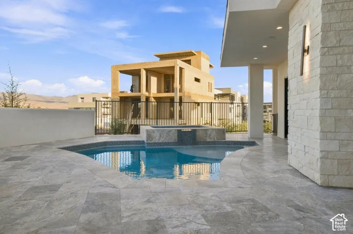 Curved swimming pool with an integrated spa, surrounded by extensive stone-tiled decking