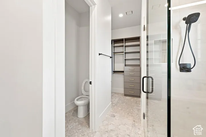 Glass-enclosed shower with matte black fixtures, custom built-in shelving, organized drawers, and light-toned flooring