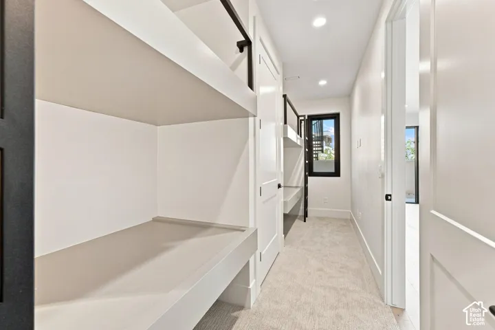 Built-in bunk beds with integrated desk, recessed lighting, neutral carpeting, and a dark-framed window