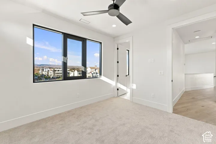 Expansive window with black trim, recessed lighting, ceiling fan, white paneled walls, and light-toned carpeting