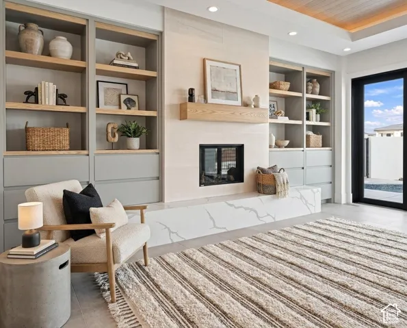 Built-in shelving with wood-finish accents, integrated fireplace with a stone hearth, recessed ceiling lighting, and a full-light exterior door
