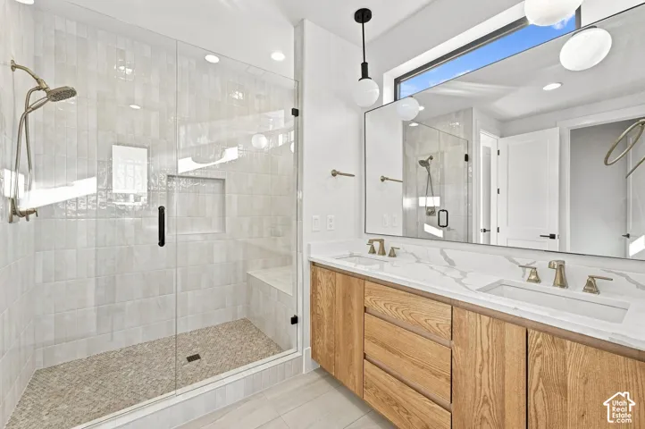 Dual vanity with wood-finish cabinetry and white countertops, large frameless mirror, glass-enclosed shower with tile surround and built-in bench, and a transom window