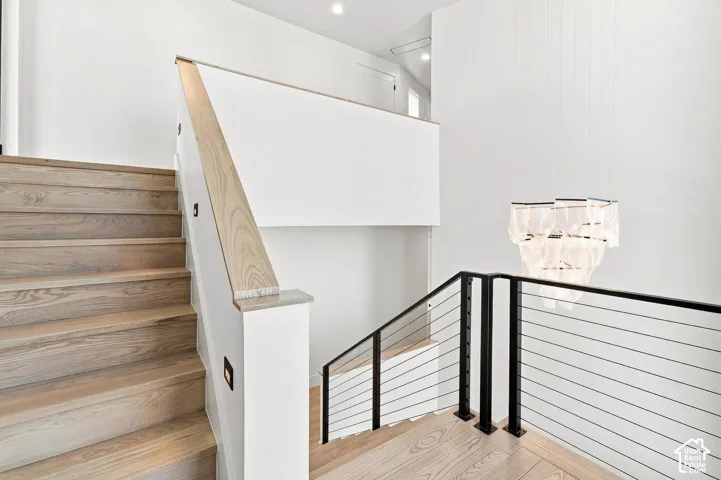 Light wood-finish staircase with recessed step lighting, modern cable railing with black posts, and a decorative multi-tiered light fixture