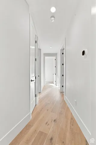 Recessed ceiling lighting illuminates a hallway with wood-finish flooring and white paneled doors