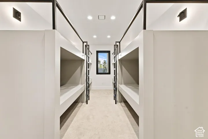 Built-in bunk beds with integrated ladders, recessed ceiling lighting, wall-mounted sconces, and neutral-toned carpeting
