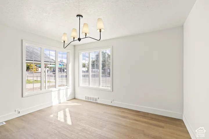 Spacious room featuring multiple windows, a contemporary chandelier, light wood-finish flooring, and white painted walls