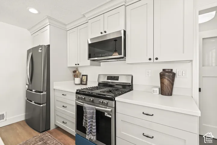Kitchen featuring white cabinetry, stainless steel appliances, light-toned countertops, and wood-finish flooring