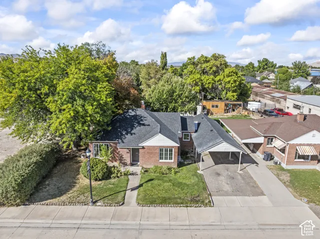 Brick-clad residence with a dark shingle roof, featuring a covered carport, manicured lawn, and mature trees