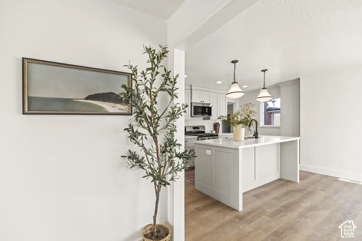 Light wood-finish flooring, white walls, kitchen island with a white countertop, two pendant lights, and white cabinetry