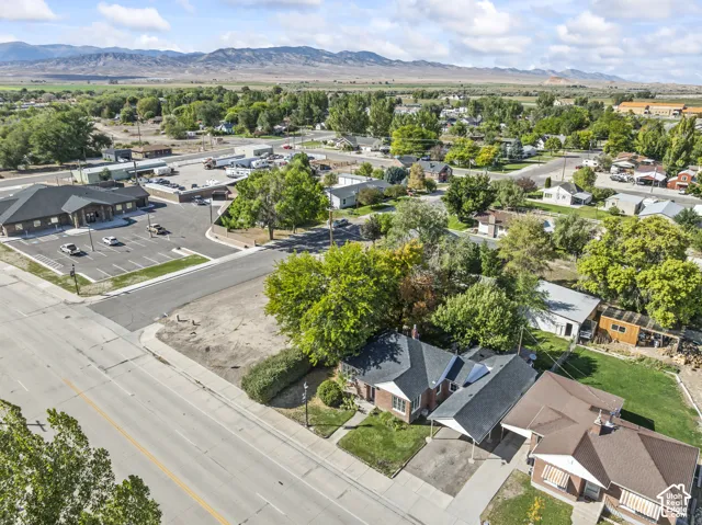 Residential property with a carport, mature trees, and a landscaped lawn, situated near a commercial building with ample parking