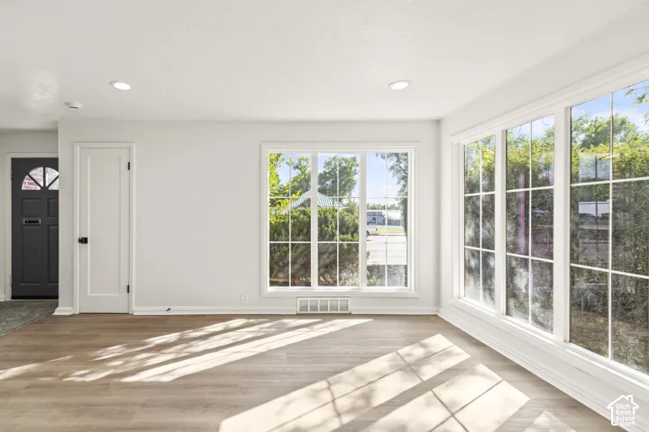 Expansive windows with white trim, wood-finish flooring, recessed ceiling lighting, and a dark paneled entry door with a decorative transom