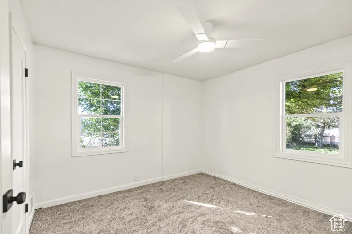 White walls, two large windows, modern ceiling fan, and grey carpet flooring