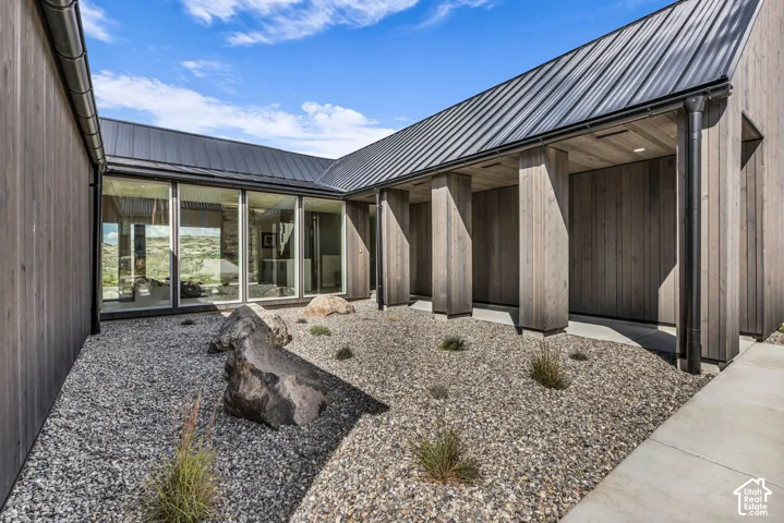 Exterior featuring vertical wood-clad siding, a dark metal roof, and a gravel courtyard with natural rock elements