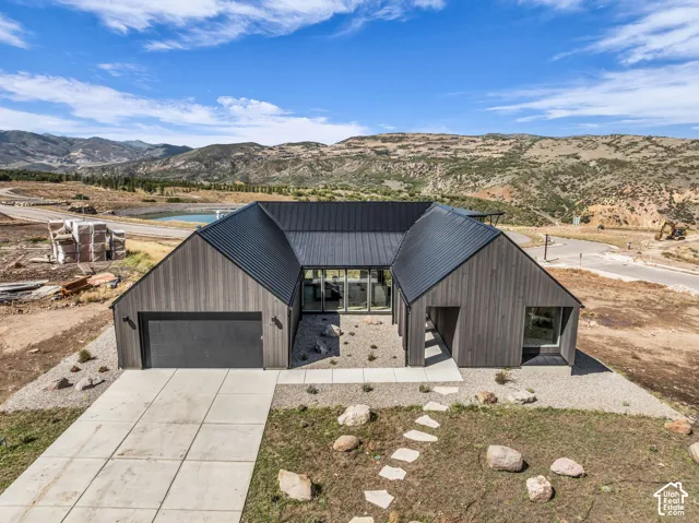 Modern exterior with a dark metal roof and wood-look siding, featuring a two-car garage and a concrete driveway