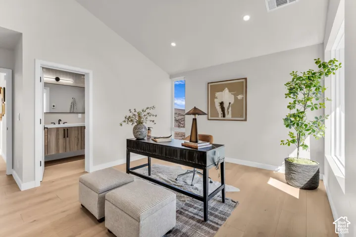 Vaulted ceiling, light wood-finish flooring, recessed lighting, vertical window, and a white vanity with wood-finish cabinetry