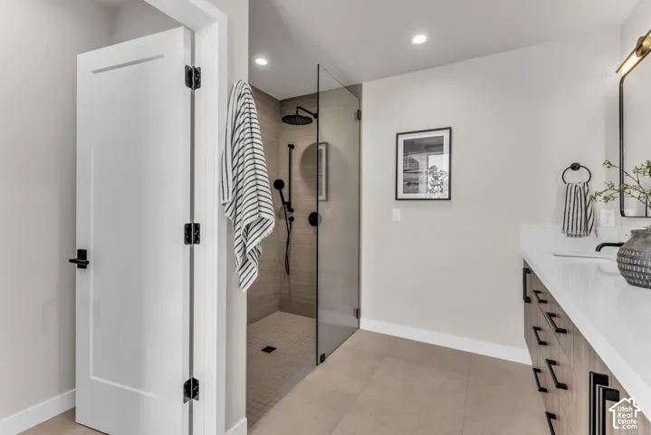 Walk-in shower with clear glass enclosure and dark-finish fixtures, single vanity with wood-finish cabinetry, quartz countertop, and overhead sconce
