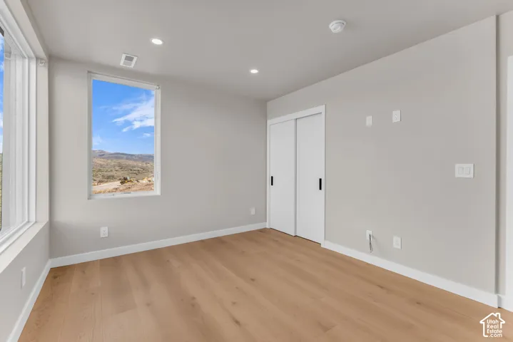 Wood-finish flooring, two large windows, white sliding closet doors, recessed ceiling lighting, and a neutral wall color