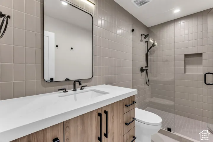 Bathroom featuring a wood-finish vanity with a white countertop, an integrated sink, a rectangular mirror, and a tiled shower with a niche
