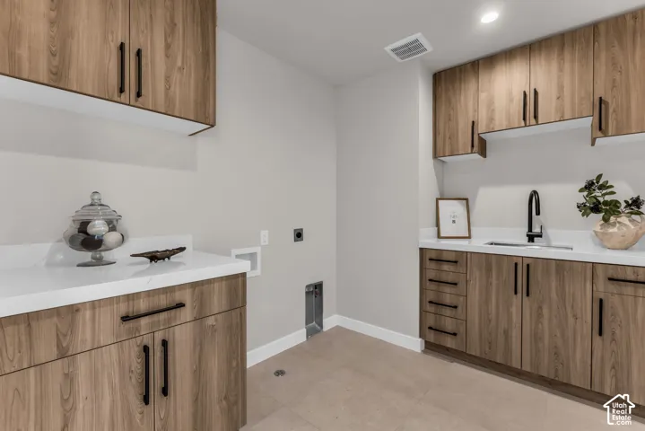 Laundry area featuring extensive wood-finish cabinetry, white countertops, an integrated sink, and a matte black faucet