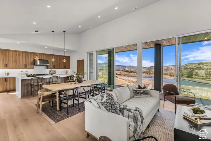 Vaulted ceilings with recessed lighting, wood-finish flooring, kitchen featuring wood cabinetry and stainless steel range hood, long island with bar seating, and expansive sliding glass doors