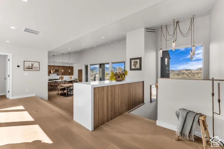 Light wood-finish flooring throughout, recessed ceiling lighting, a modern chandelier, and a built-in wood-finish half-wall partition