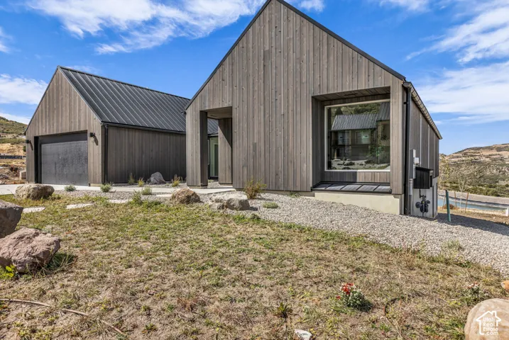 Modern architectural design featuring vertical wood siding, a standing seam metal roof, a large picture window, and an attached garage with a dark finish door