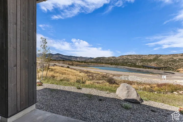 Wood-paneled exterior siding with a concrete foundation, overlooking a landscape featuring a body of water, distant mountains, and natural rock elements