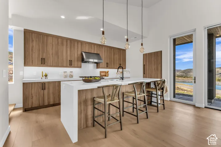 Kitchen featuring wood-finish cabinetry, white countertops, a stainless steel range hood, and an island with pendant lighting