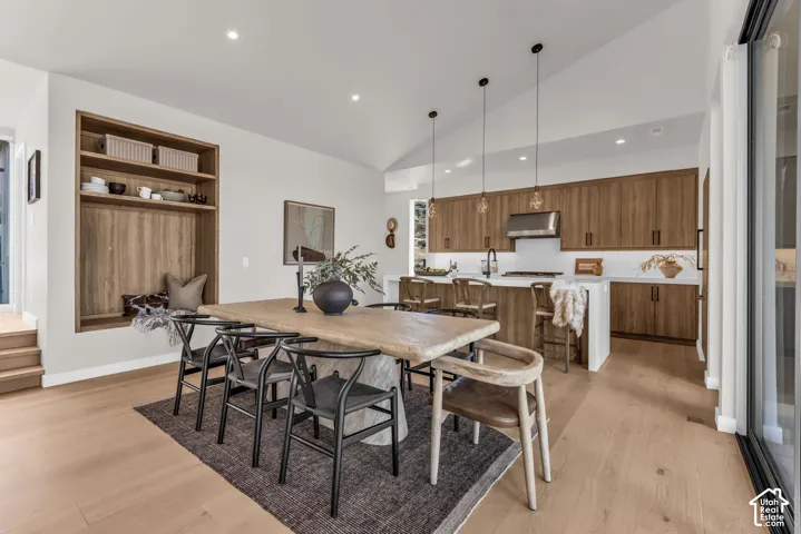 Vaulted ceilings, wood-finish flooring, built-in shelving, wood-finish cabinetry, and a kitchen island with pendant lighting
