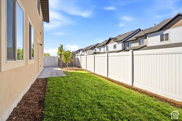 Manicured lawn, paved patio, mature tree, durable privacy fencing, and stucco exterior
