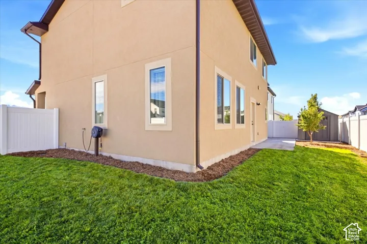 Expansive lawn area with mature landscaping, stucco exterior, multiple windows, and a paved patio