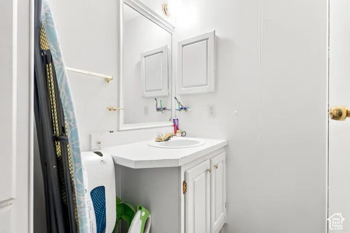 White vanity with integrated sink, gold-finish hardware, wall-mounted mirror, and cabinet storage