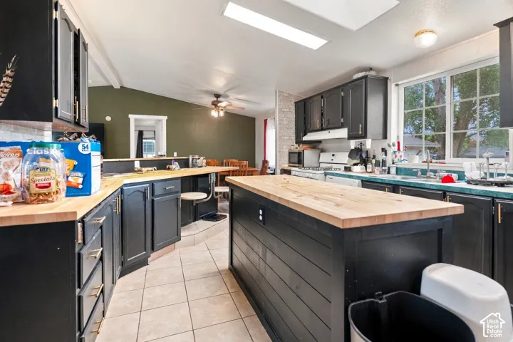Kitchen featuring black cabinetry, light wood-finish countertops, a central island with a wood-finish top, and tiled flooring