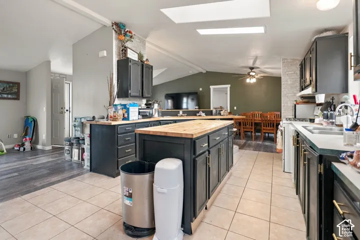 Kitchen featuring dark cabinetry, a center island with a wood-finish countertop, light-toned tile flooring, and vaulted ceilings with skylights