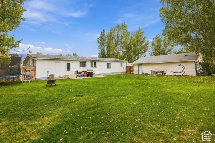Expansive green lawn with a white-sided residence, a detached garage, and a concrete patio