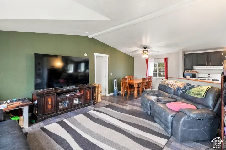 Open concept living area featuring wood-finish flooring, a vaulted ceiling, and a ceiling fan