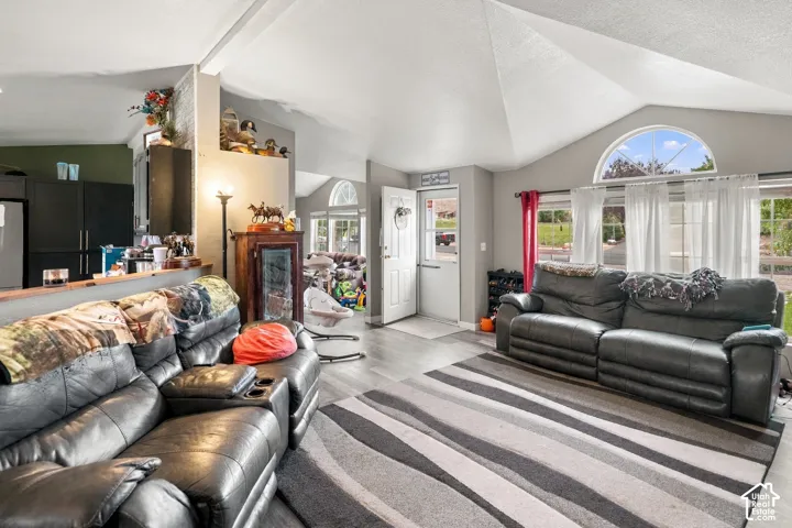 Vaulted ceilings, wood-finish flooring, a functional kitchen pass-through, and a prominent arched window above a large picture window