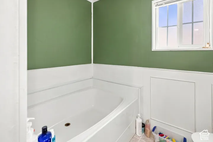 Built-in bathtub, paneled wainscoting, green wall finish, and a white-framed window