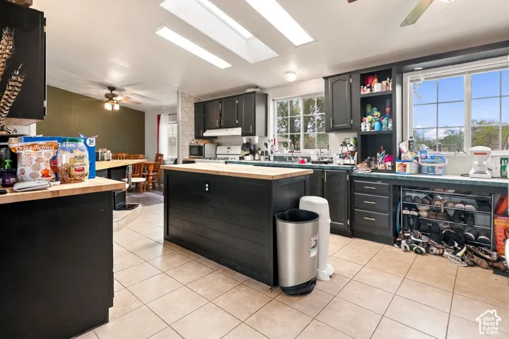 Kitchen featuring a central island with wood-finish countertop, dark cabinetry, tile flooring, and multiple windows